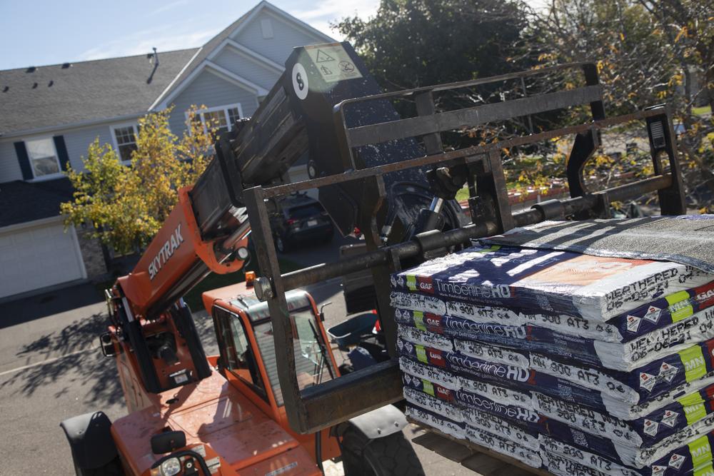 Telehandler delivering GAF Timberline HDZ bundles to a townhome roof